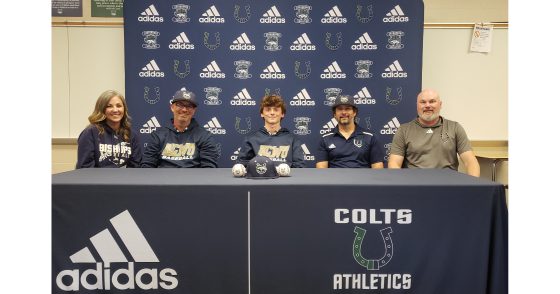 Young athlete signs an NIL deal at a press table flanked by coaches and family, with an Adidas backdrop and Colts Athletics branding behind them.